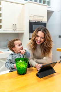 Young mother and toddler son share popcorn and smiles while watching a tablet in their modern