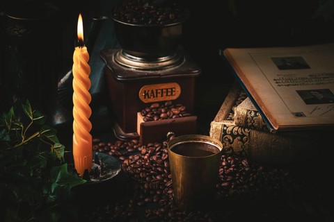 Cosy scene with old coffee grinder, steaming coffee and burning candle in a dark atmosphere