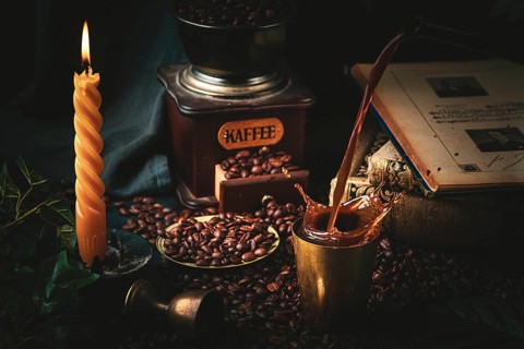 Snapshot of pouring coffee with spritzer, candle, coffee grinder and old books