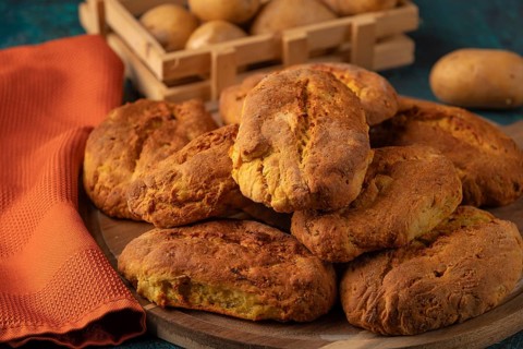 Freshly baked potato rolls with golden brown crust on a wooden board, potatoes in the background
