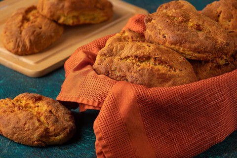Fresh potato rolls in a basket with orange cloth, some presented on a wooden board