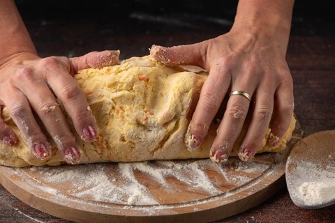 Hands knead a large lump of dough on a floured wooden board