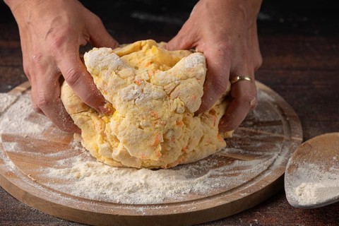 Two hands knead dough on a floured wooden board in the kitchen