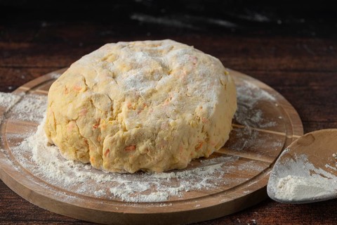 A lump of dough covered with flour on a wooden board in a dark kitchen