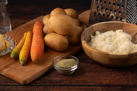 Potatoes, carrots and cheese on a table with spices and a grater