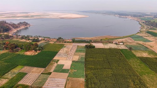 Aerial view of cultivated farmland along the riverbank, with patchwork fields stretching toward a