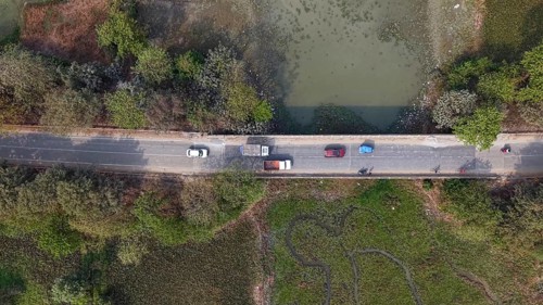 Aerial top-down view of vehicles traveling along a rural road bordered by wetlands and dense