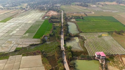 Aerial view of a rural road cutting through patchwork agricultural fields and ponds in the