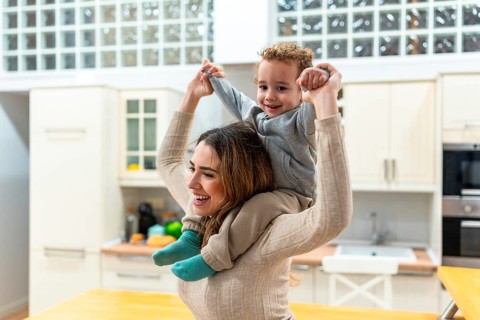 Happy mother giving her cheerful son a piggyback ride at home, celebrating family joy, childhood