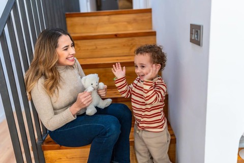 Mother and toddler sitting happily on wooden stairs, engaging in playful interaction with a small