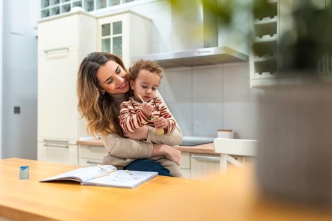 Caring mother smiling and embracing her young child while sitting at a kitchen table, bonding over