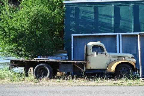 An abandoned old truck on the side of the road next to a green wall and trees, Mitchell, Oregon,