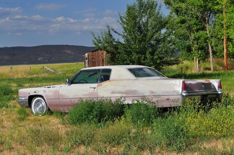 Abandoned old car, Cadillac classic car, in a meadow next to a small wooden building, Unity,