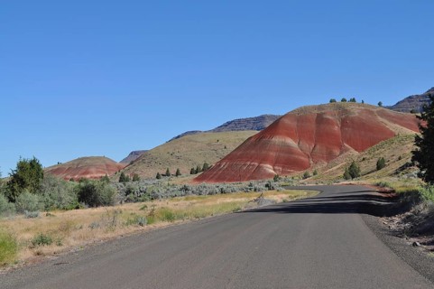 Asphalt road leads through the Painted Hills landscape under clear skies, John Day Fossil Beds