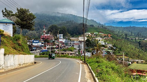 View of a curvy road in a village with hills and green countryside under a cloudy sky, The road on