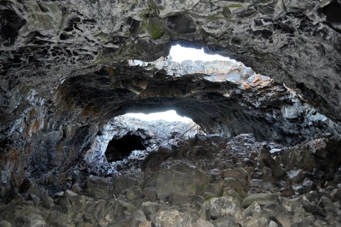 Rocky lava cave opening with irregular walls through which bright light shines in, Craters of the