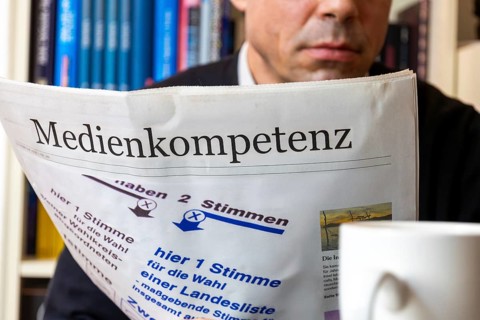 Man reads (symbolic) newspaper with the headline MEDIA COMPETENCE