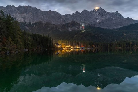A stunning night view of Eibsee, surrounded by the Bavarian Alps The illuminated village reflects