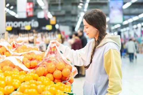A woman is seen selecting oranges from a fresh produce section in a bustling supermarket, examining