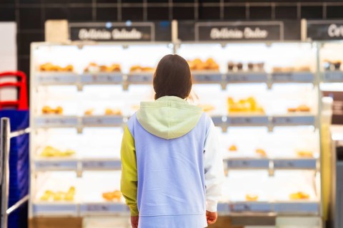 Back view of an unrecognizable woman standing in front of the bakery section in a supermarket,