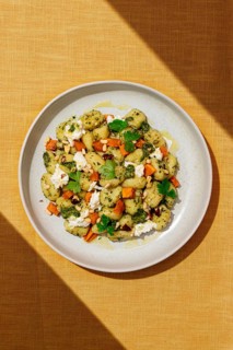 Top view of a gourmet dish featuring Italian gnocchi dressed with green pesto sauce, sprinkled with