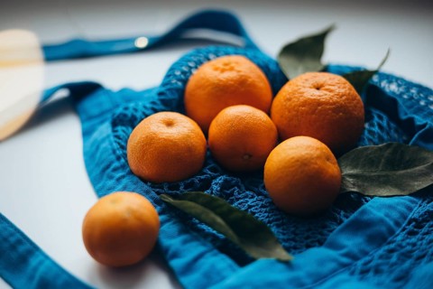 Tangerines rest in a vibrant blue string bag, highlighted by soft natural light, surrounded by