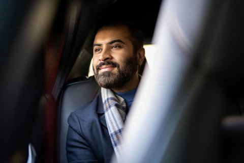 An Indian businessman in a cozy winter outfit looks contemplatively out of a car window, showcasing