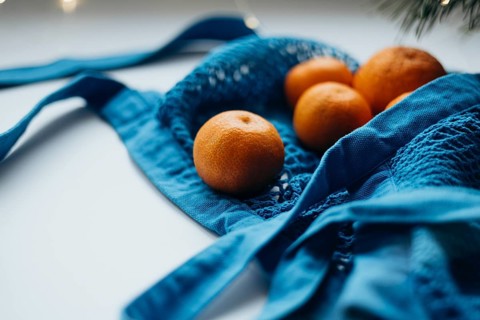 Close-up view of ripe tangerines neatly tucked inside a vibrant blue string bag, set against a