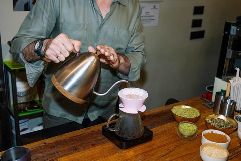A barista carefully pours hot water into a dripper, crafting specialty coffee with precision.