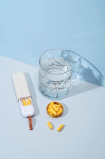 Top view of a white pillbox with orange capsules, a crystal glass filled with water, and extra