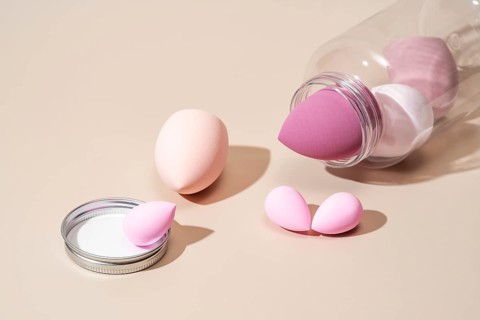 A collection of pink and beige cosmetic sponges arranged on a neutral beige background, ideal for