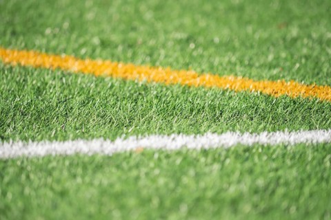 A detailed close-up of green artificial turf with bold white and yellow lines, capturing the
