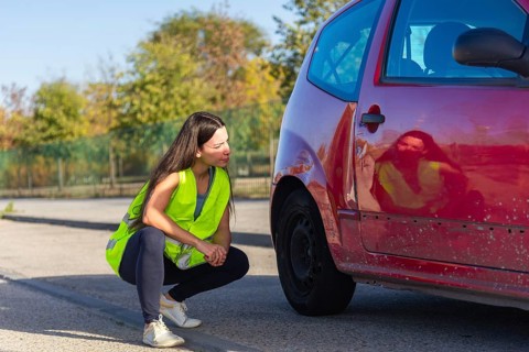 A woman in a high-visibility vest examines the damage on a red car after a minor accident The scene