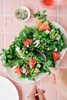 Top view of cropped unrecognizable hands eating vibrant salad featuring ruccola, watermelon,