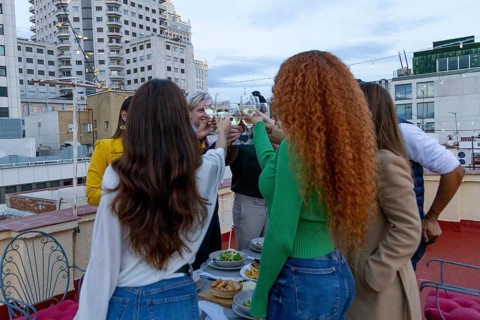 A lively group of friends celebrates on a rooftop, raising glasses in a toast Surrounded by city