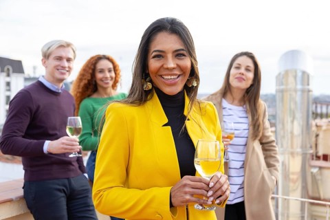 A group of cheerful friends enjoying a casual gathering on a rooftop, holding glasses of wine The