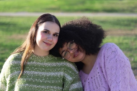 Two friends, one with long hair and the other with curly hair and glasses, wearing cozy sweaters,