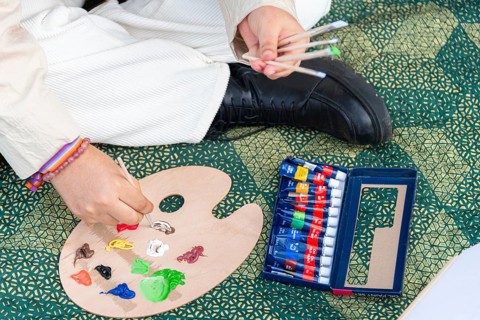A close up of a young black woman preparing a wooden palette with colorful paint tubes and brushes