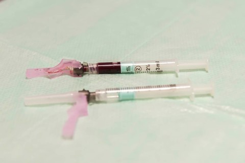 A close-up image of medical syringes filled with blood, laid on a sterile aqua-colored surface,