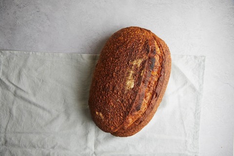 Top view of a freshly baked sourdough bread with a crispy crust, resting on a white linen cloth,