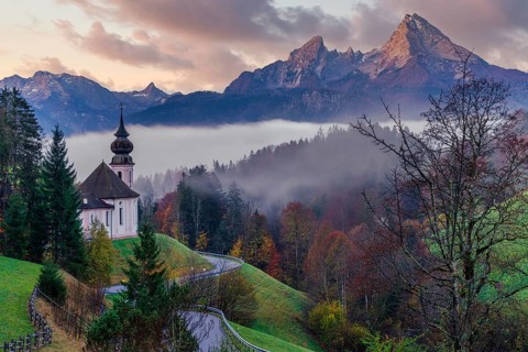 The picturesque Maria Gern Church is nestled among vibrant autumn foliage with the majestic