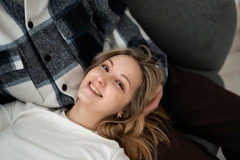 A young woman with a cheerful smile lying next to her cropped unrecognizable partner. She appears