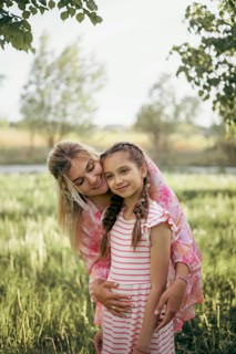 A mother gently embraces her daughter in a lush green field, radiating love and warmth Their smiles