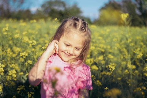 A little girl in a pink outfit smiles as she admires the flowers around her Her innocence and
