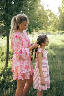A loving mother gently braids her daughter's hair in a sunlit park. The tender moment captures