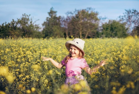 A little girl in a pink dress twirls happily among yellow flowers, embracing the beauty of nature