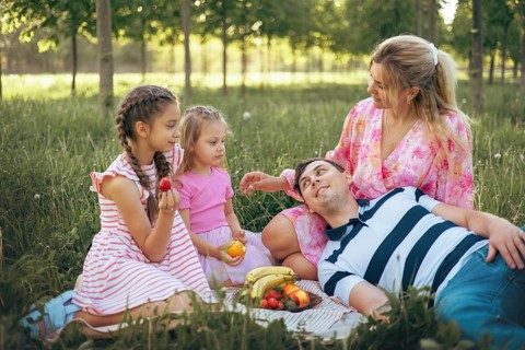 A loving family relaxes on the grass during a picnic, surrounded by nature. With fresh fruits and