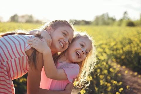 Two girls sisters play happily together in nature on a flowering field in summer