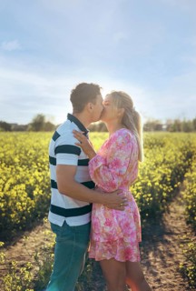 A loving couple embraces and shares a kiss in a golden flower field during sunset. The warm