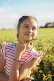 A young girl in a striped dress enjoys a peaceful moment in a blooming field, holding wildflowers